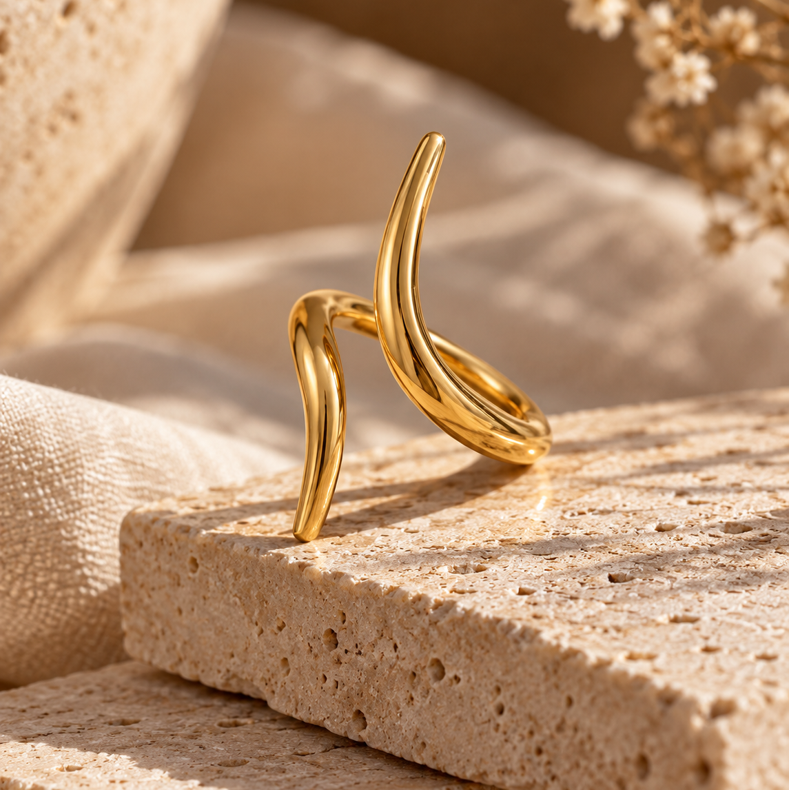 Reneax and Company minimalist gold-tone spiral wrap ring with a polished finish resting on a textured stone block.