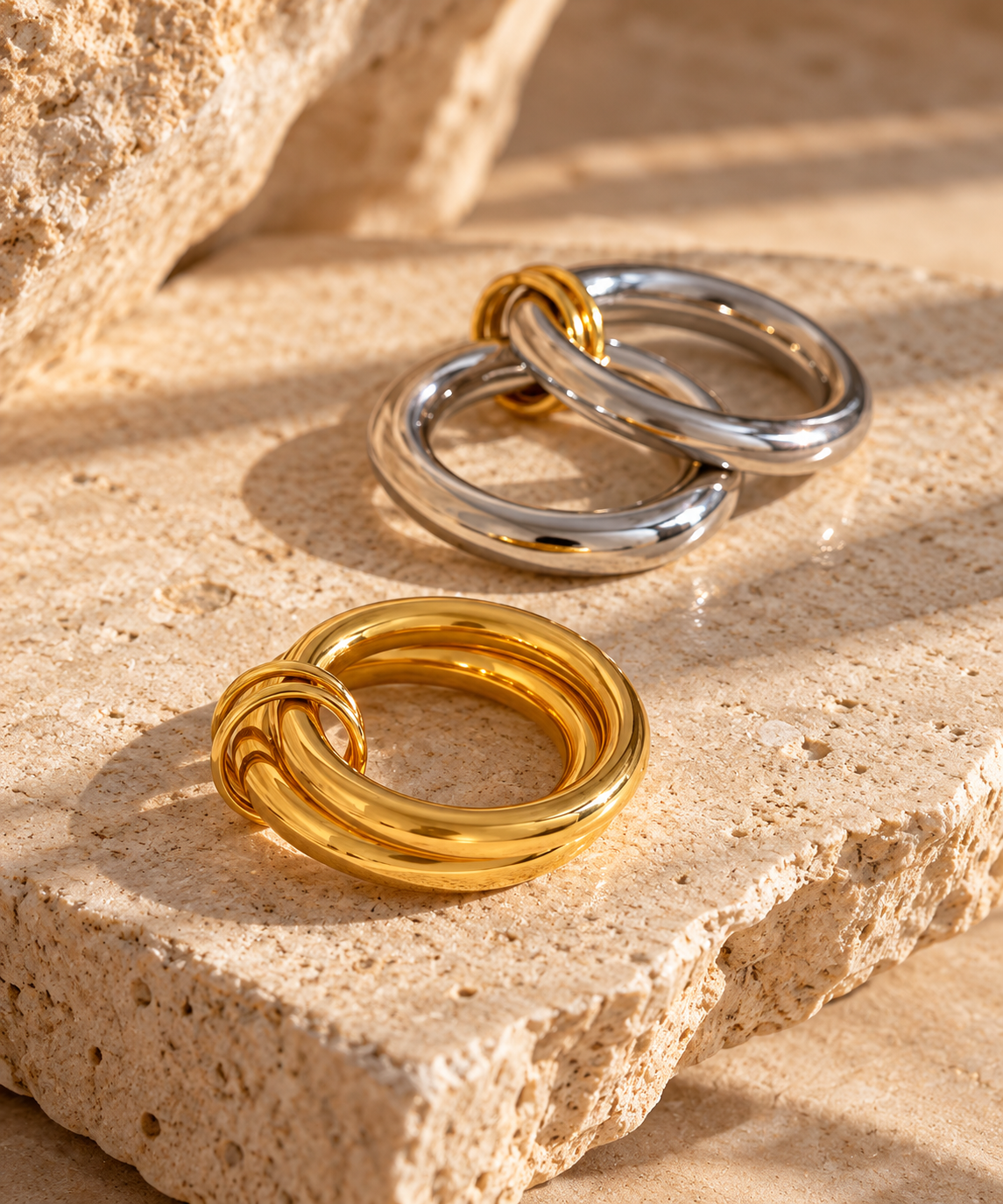 Reneax and Company interlocking mixed metal band rings in gold and silver tones resting on a textured stone surface.
