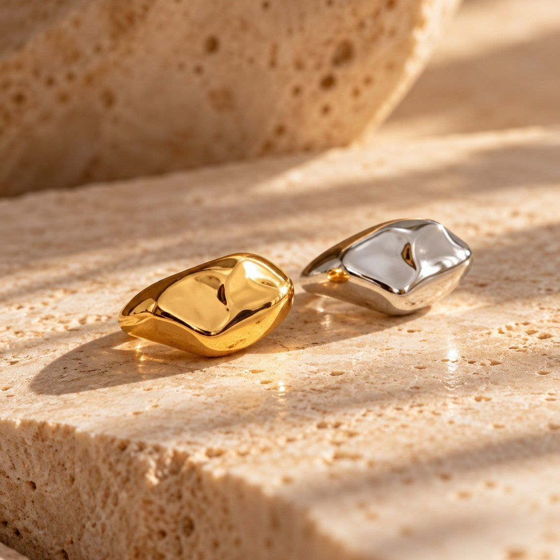 Reneax and Company gold and silver molten sculptural statement rings on a textured stone surface