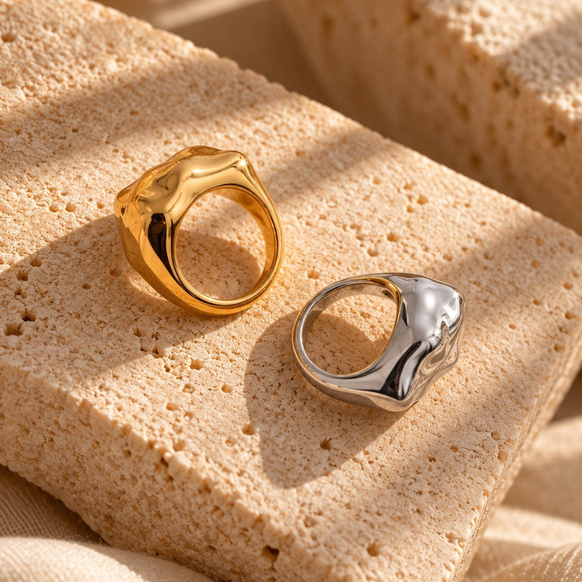 Reneax and Company gold and silver molten-style sculptural statement rings resting on a textured stone block.