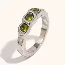 Reneax and Company three stone statement ring with a molten silver texture and three round-cut green gemstones.